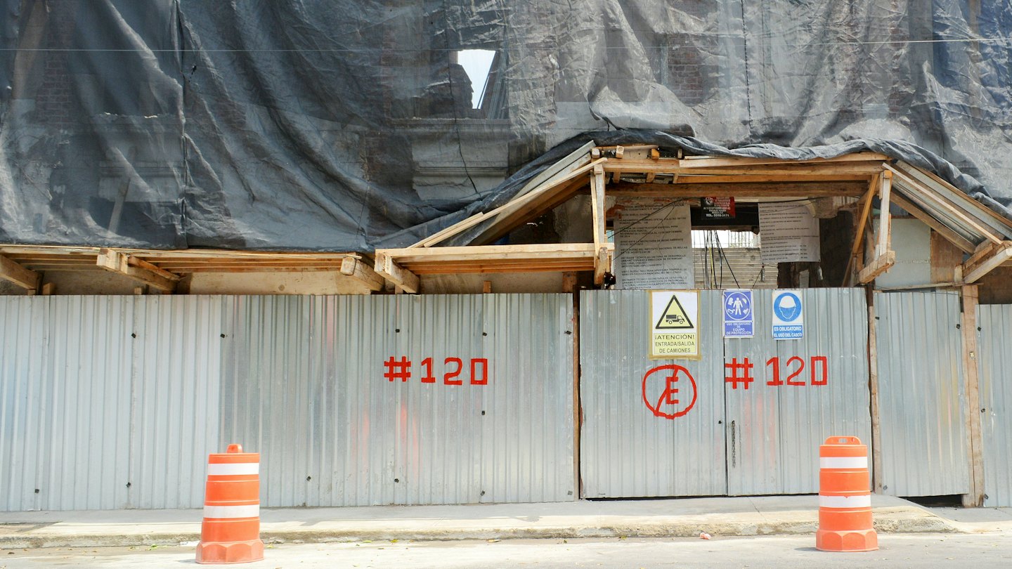 Baustelle mit Gerüsten und Sicherheitsbeschilderung auf dem Bürgersteig.